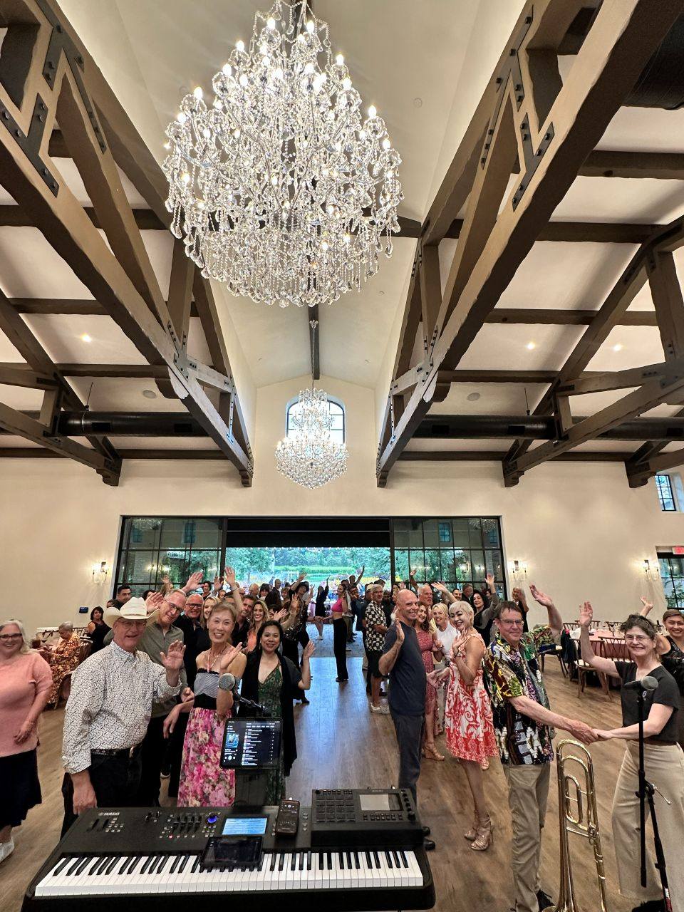 A full room of guests raising their hands toward the band beneath crystal chandeliers at a Positive Energy event