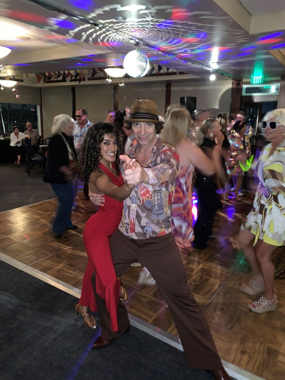 A couple dancing together, the woman in a red dress, on a lively social dance floor