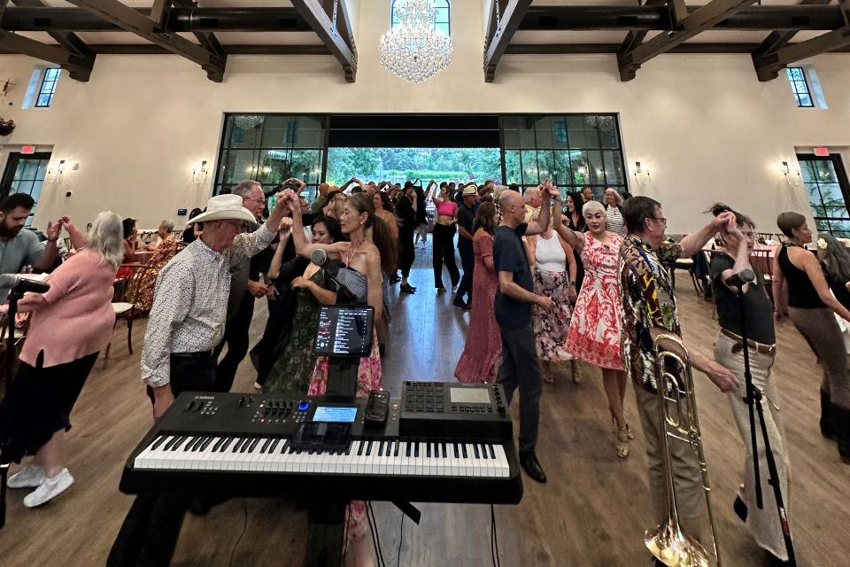 Couples in dance hold under a crystal chandelier at an elegant garden-view reception